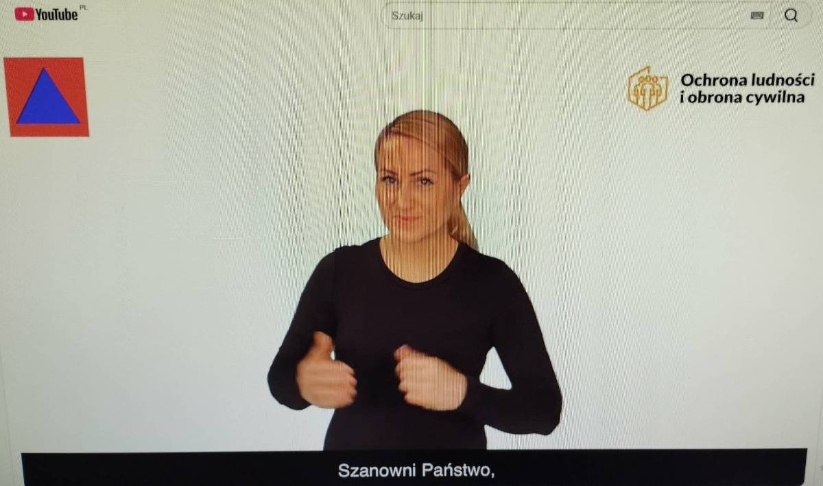 Na zdjęciu kadr z Poradnika bezpieczeństwa na You Tube przetłumaczonego na język migowy . W kadrze lektorka w czarnym kostiumie tłumaczy tekst poradnika