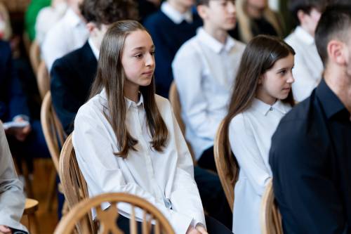 Młodzież galowo ubrana siedzi na jasnych krzesłach