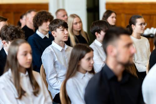 Młodzież galowo ubrana siedzi na jasnych krzesłach