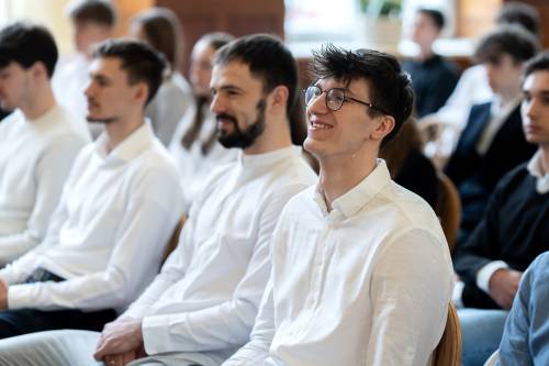 Młodzież galowo ubrana siedzi na jasnych krzesłach