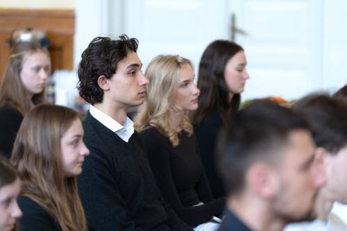 Młodzież galowo ubrana siedzi na jasnych krzesłach