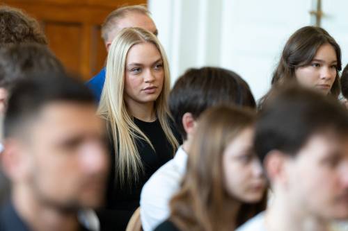 Młodzież galowo ubrana siedzi na jasnych krzesłach
