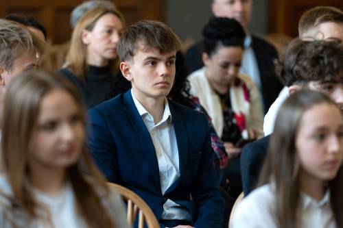 Młodzież galowo ubrana siedzi na jasnych krzesłach