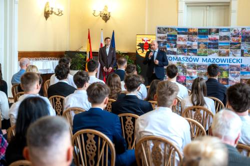 Młodzież galowo ubrana siedzi na jasnych krzesłach