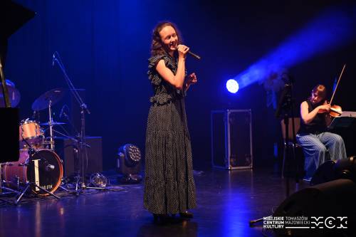 Na zdjęciu koncert zespołu Arete z wokalistką przy mikrofonie. Kolorowe światła sceniczne. Na drugim planie pozostali muzycy