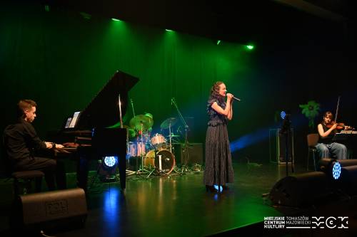 Na zdjęciu koncert zespołu Arete z wokalistką przy mikrofonie. Kolorowe światła sceniczne. Na drugim planie pozostali muzycy