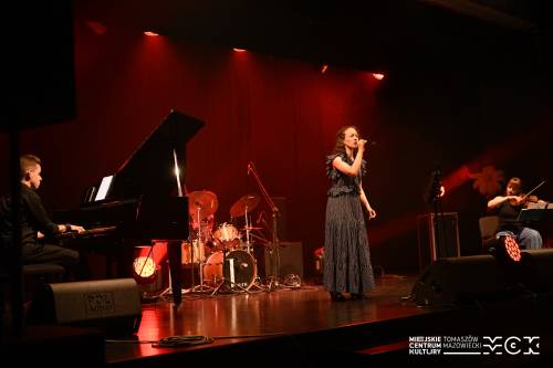 Na zdjęciu koncert zespołu Arete z wokalistką przy mikrofonie. Kolorowe światła sceniczne. Na drugim planie pozostali muzycy