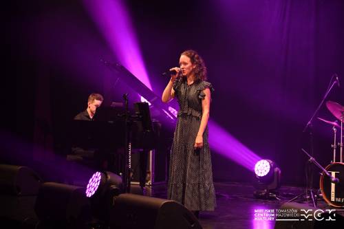 Na zdjęciu koncert zespołu Arete z wokalistką przy mikrofonie. Kolorowe światła sceniczne. Na drugim planie pozostali muzycy